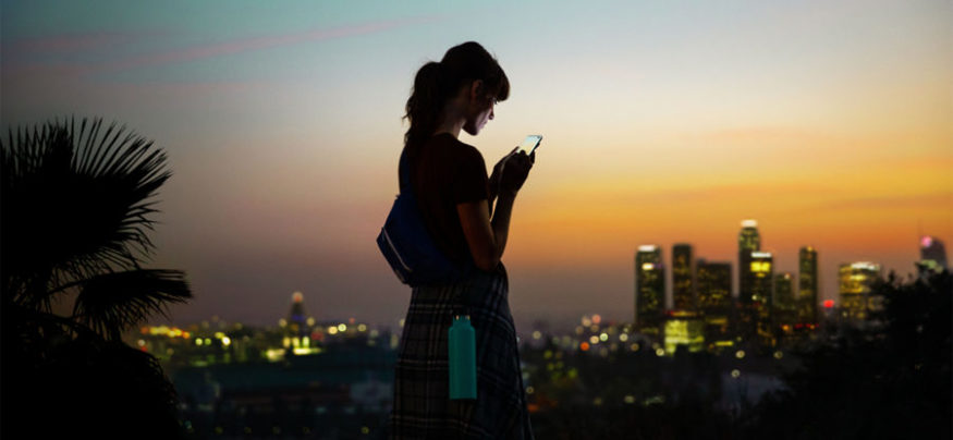 Woman using a 5G-enabled smartphone outside a connected cityscape