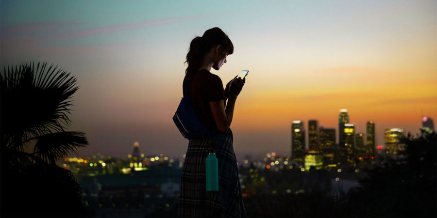 Woman using a 5G-enabled smartphone outside a connected cityscape