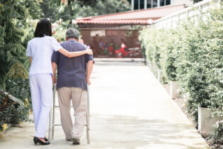 A caregiver strolls with a patient using a walker
