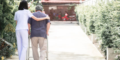 A caregiver strolls with a patient using a walker