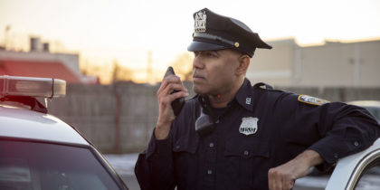 Police officer using push-to-talk smartphone next to cruiser