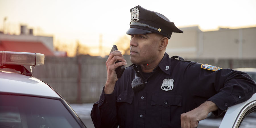 Police officer using push-to-talk smartphone next to cruiser