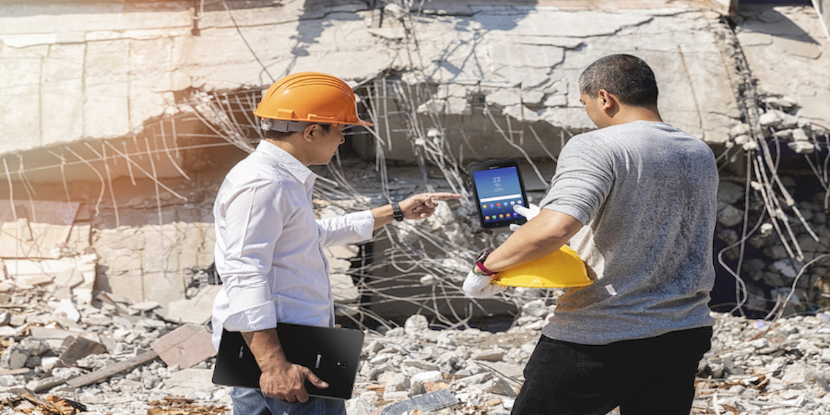 Two workers with hard hats use a tablet in the field