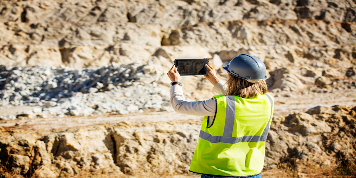 A worker in a safety vest and hard hat uses a tablet to take a photo