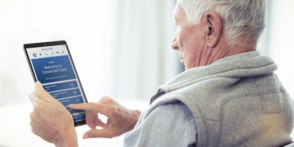 An older man uses a Samsung tablet to access a remote healthcare app from home