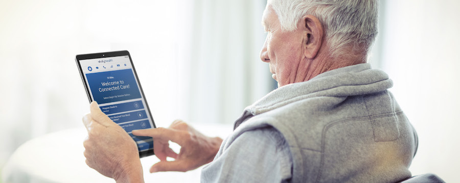 An older man uses a Samsung tablet to access a remote healthcare app from home