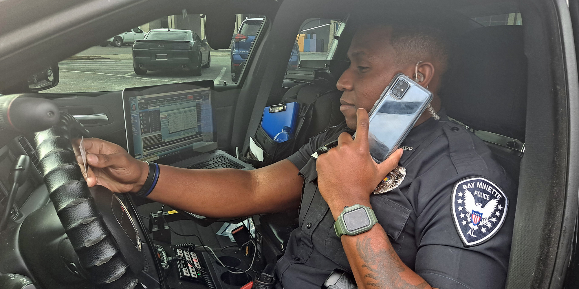 Bay Minette police officer in cruiser speaking on Samsung smartphone