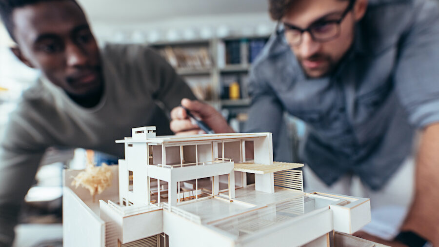 Close up shot of scale model house on table with architects. Two architects making architectural model in office together.