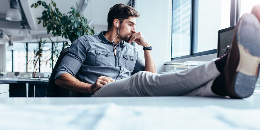 Businessman sitting in office and listening music. Thoughtful man sitting with feet on table in office.