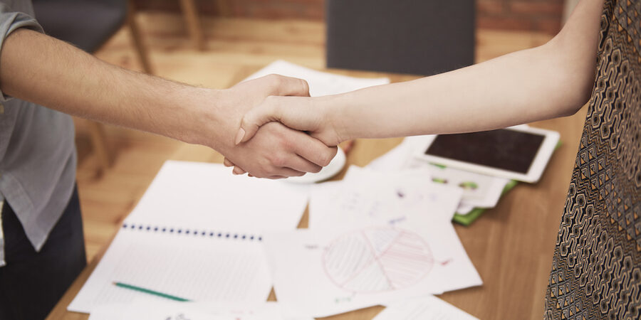 Business employees shaking hands over table with notebooks