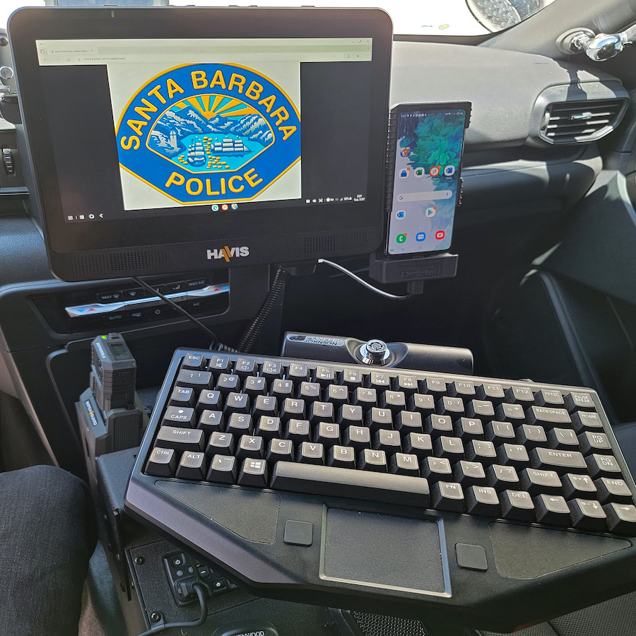 Inside a police patrol vehicle, the center dashboard contains a mounted computer monitor, keyboard and smartphone.