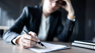 A close-up shot of a businessperson's hand writing on a paper form.