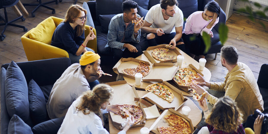 Group of male and female co-workers sharing pizza together in comfortable chairs in office