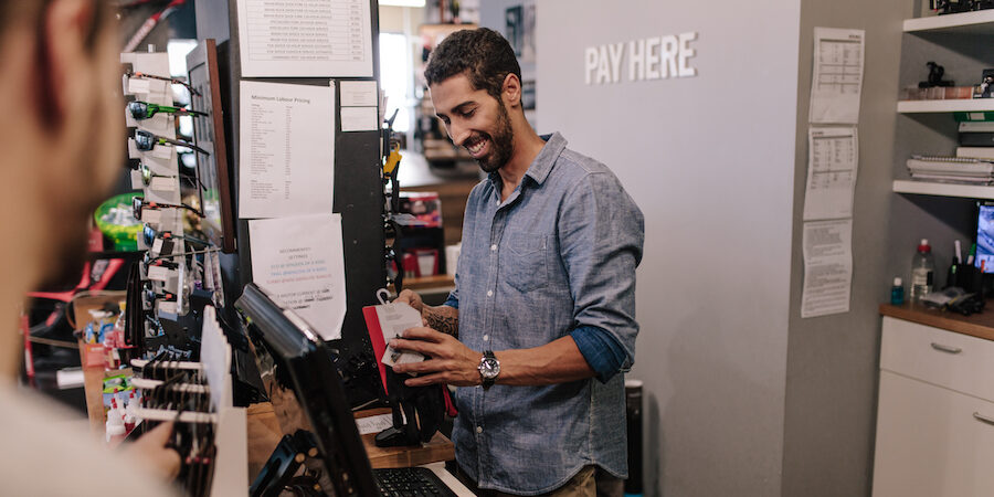 Smiling sports shop owner preparing bill at the payment counter.