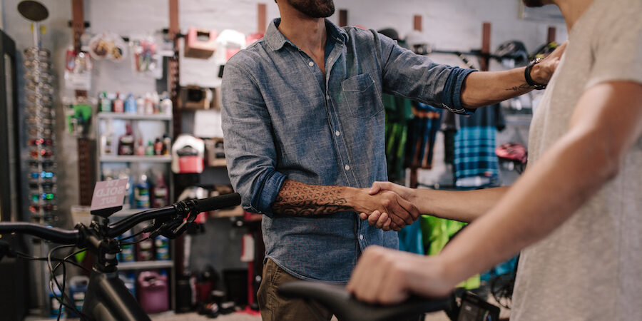 Cropped shot of shop owner giving a handshake to a customer after selling a bicycle.