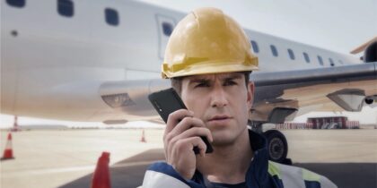 Airport worker in front of plane on tarmac speaking on Samsung rugged smartphone