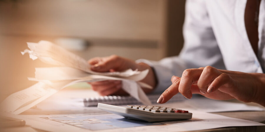 Close up of accountant holding bills and working on calculator in the office.